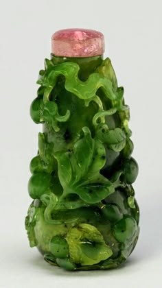 a glass bottle with green and pink decorations on the top, sitting in front of a white background