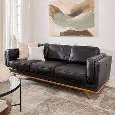 a black leather couch sitting in a living room next to a painting on the wall