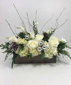 an arrangement of white flowers and greenery in a wooden vase with silver ornaments on top