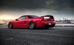 a red sports car parked in front of a large body of water under a cloudy sky