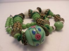 a green beaded bracelet with beads and bells on it's end, sitting on a white surface