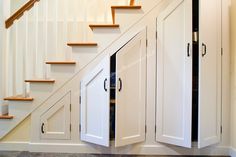 an under stair storage area with white cabinets and wood stairs in a home setting that also has hardwood flooring