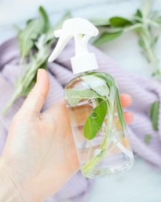 a hand holding a spray bottle filled with water and green leaves next to a purple towel