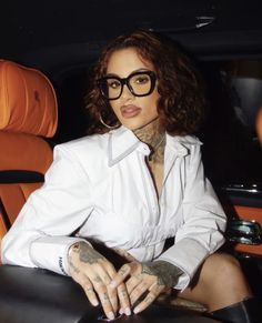 a woman sitting in the back of a car wearing black rimmed glasses and a white shirt