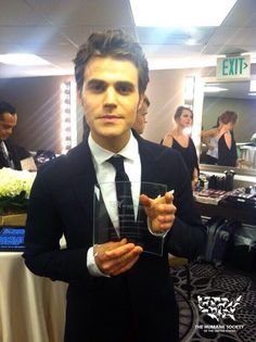 a man in a suit and tie holding up an award at a formal event with people in the background