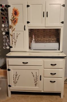 a white cabinet with sunflowers painted on the doors and drawers, next to a sewing machine