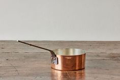 an old fashioned copper pan with a wooden handle on a wood table, ready to be used for cooking