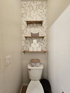 a small bathroom with a toilet and shelving above the toilet seat is decorated in neutral tones