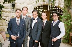 a group of men standing next to each other in suits and ties holding wine glasses