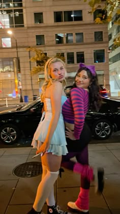 two young women dressed in costumes posing for the camera on a city street at night