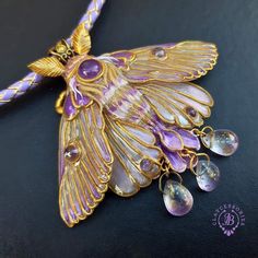 a purple and gold necklace with a large butterfly on it's back, sitting on a black surface