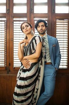 a man and woman standing next to each other in front of wooden shuttered windows