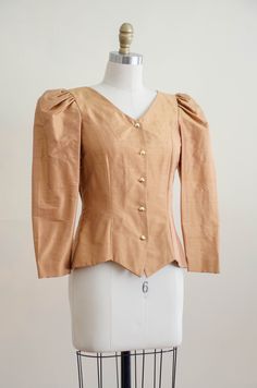 A homemade golden tan jacket, with puffed shoulders, gold faceted buttons, and good tailoring. It is unlined and light enough to be worn as a blouse. ☛ m e a s u r e m e n t s ☚ Bust: 32 Waist: 28 Shoulders: 13.5 Length: 21 ☛ d e t a i l s ☚ Era: 1990s Material: polyester Condition: excellent ☛ v i s i t t h e s h o p ☚ https://etsy.me/2Nd23kg ☛ instagram ┇ poppycockvintage ☛ facebook ┇ poppycockvintage Puff Sleeve Jacket, Gold Ear Climbers, Winston Salem Nc, Golden Tan, Gold Blouse, Tan Jacket, Blouse Price, Winston Salem, White Coat