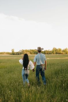 a man and woman walking through a field holding hands