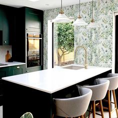 a kitchen with green and white wallpaper, bar stools, an island sink and three hanging lights