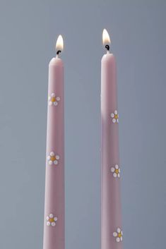 two pink candles with daisies on them against a gray background, one is lit