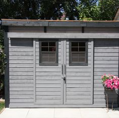 a large gray shed with two doors and flowers in the potted planter next to it