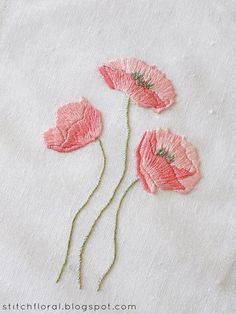 three pink flowers are embroidered onto a white cloth