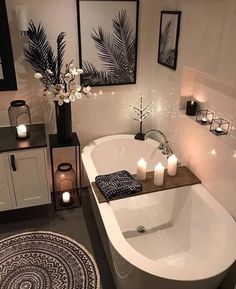 a white bath tub sitting in a bathroom next to candles and pictures on the wall