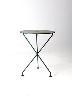 a small round table with metal legs and a green top, against a white background