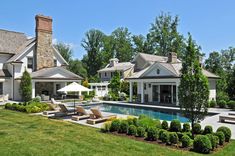 an outdoor swimming pool with lounge chairs and umbrellas in front of the house, surrounded by lush greenery