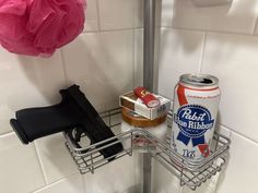 a can of beer and two cans of soda on a shower rack in a bathroom