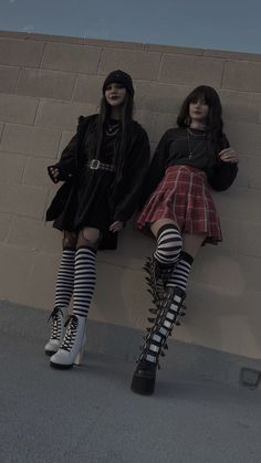 two young women dressed in punk clothing leaning against a wall