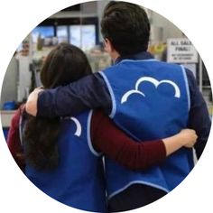 a man and woman hugging each other in front of a store counter with an advertisement on the wall behind them