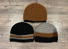 two crocheted hats sitting next to each other on a wooden floor with white and brown stripes