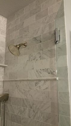 the shower head is mounted to the side of the wall with marble tiles on it