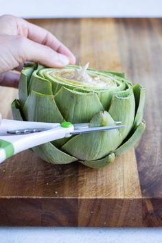 a person cutting artichoke on a wooden cutting board