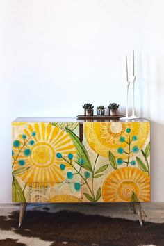 a yellow and green painted sideboard with flowers on it next to a cowhide rug