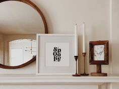 a white mantle topped with a framed drawing and two candles next to a round mirror