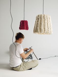 a person sitting on the ground with a remote in front of two knitted lamps