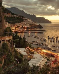 boats are docked in the water at dusk near a city with mountains and buildings on either side