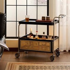 a bar cart with drinks on it in front of a large window, next to a chair and rug