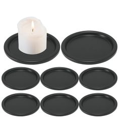 six black plates and a lit candle on a white background