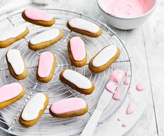 cookies with pink and white frosting on a cooling rack next to a bowl of candy