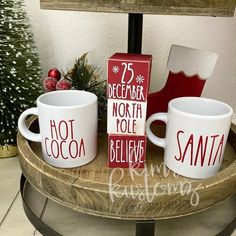 two coffee mugs sitting on top of a wooden tray next to a christmas tree