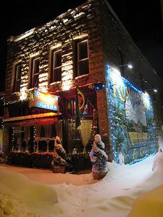 a building covered in snow at night with christmas lights on the windows and decorations all around