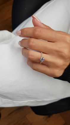 a woman's hand with a diamond ring on her finger, sitting on a white pillow