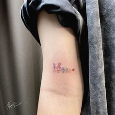 a small tattoo on the arm of a woman with three little people in different colors