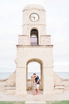 a man and woman kissing in front of a clock tower with the ocean in the background