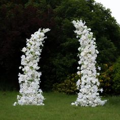 two tall white flowers sitting on top of a green grass covered field next to trees