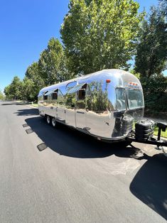 a silver airstream parked on the side of a road next to trees and bushes