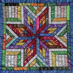 a multicolored star quilt hanging on a blue fabric wallhanger with metallic foils