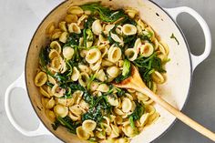 a pot filled with pasta and spinach on top of a table next to a wooden spoon