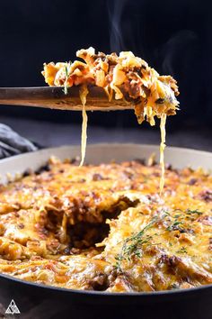 a spoon full of food being lifted from a casserole dish with meat and cheese