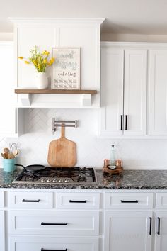 a kitchen with white cabinets and marble counter tops, including a wooden cutting board on the stove