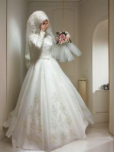 a woman in a white wedding dress is holding her hands to her face while standing against a wall